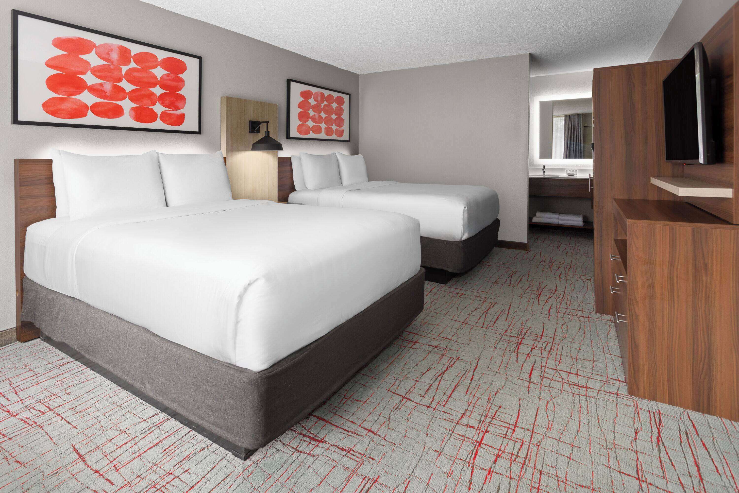 A hotel room with two beds, a TV, a desk, and artwork on the walls.