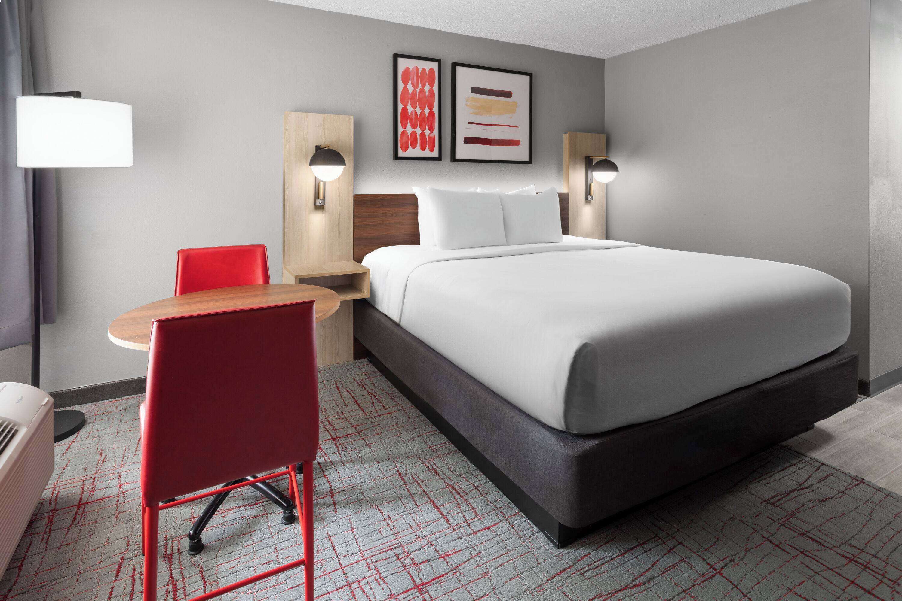 Una habitación de hotel con una cama, un escritorio, una silla y dos lámparas fijadas a la pared.