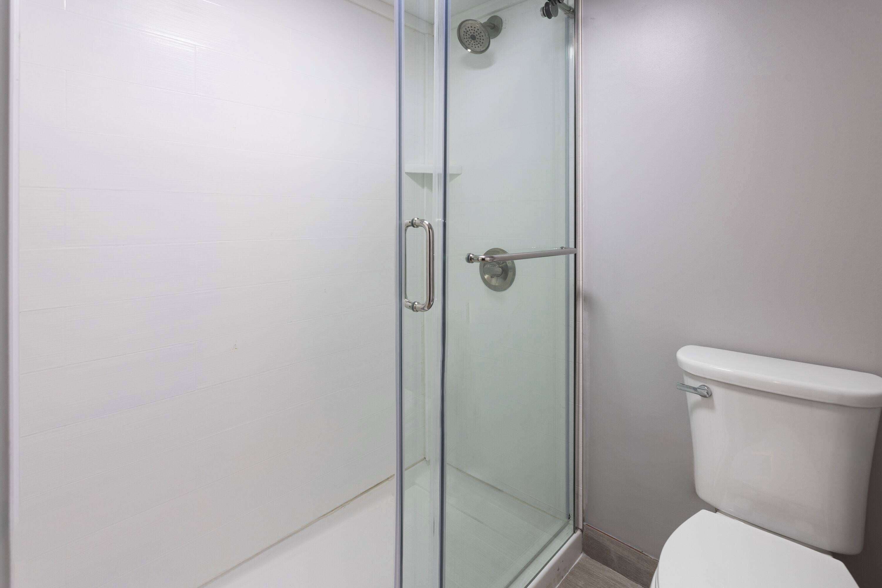 A bathroom with a glass-enclosed shower, a white toilet, and a tiled floor.