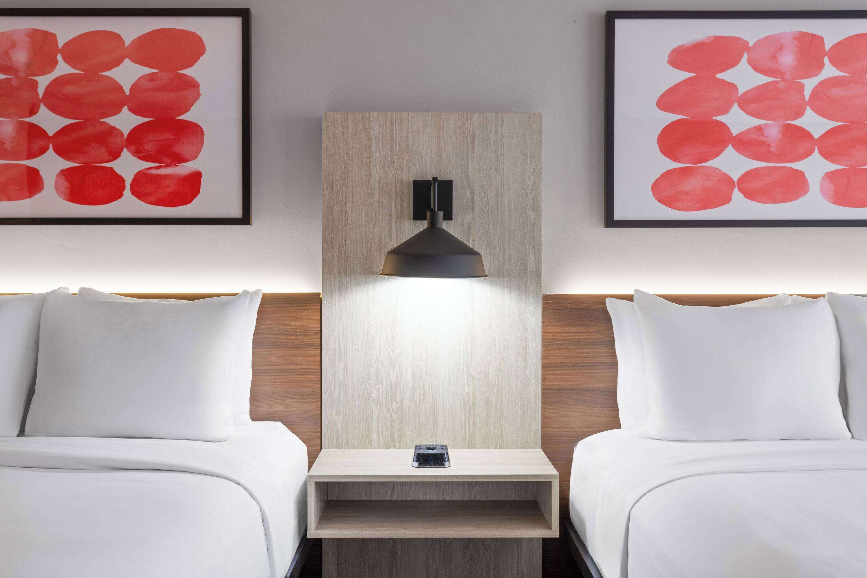 A hotel room with two beds, a nightstand, and a wall-mounted lamp.