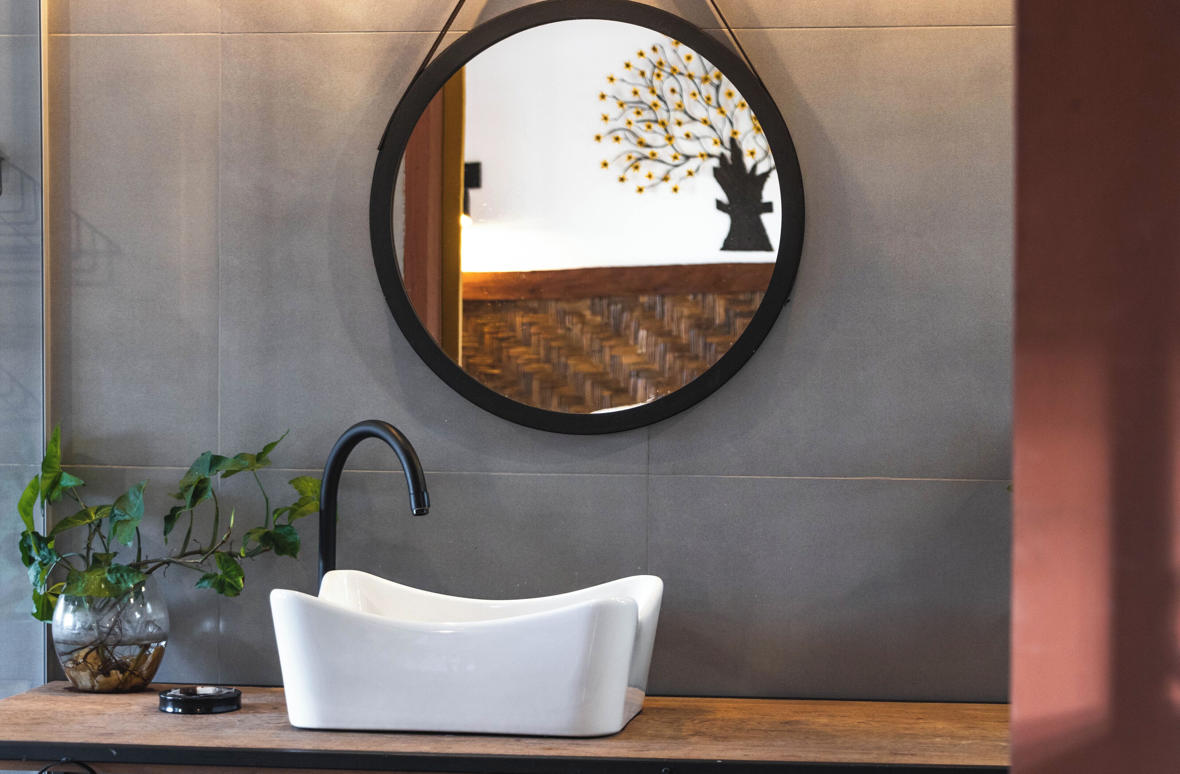 Een moderne badkamer met een ronde spiegel, een witte wastafel en een potplant.