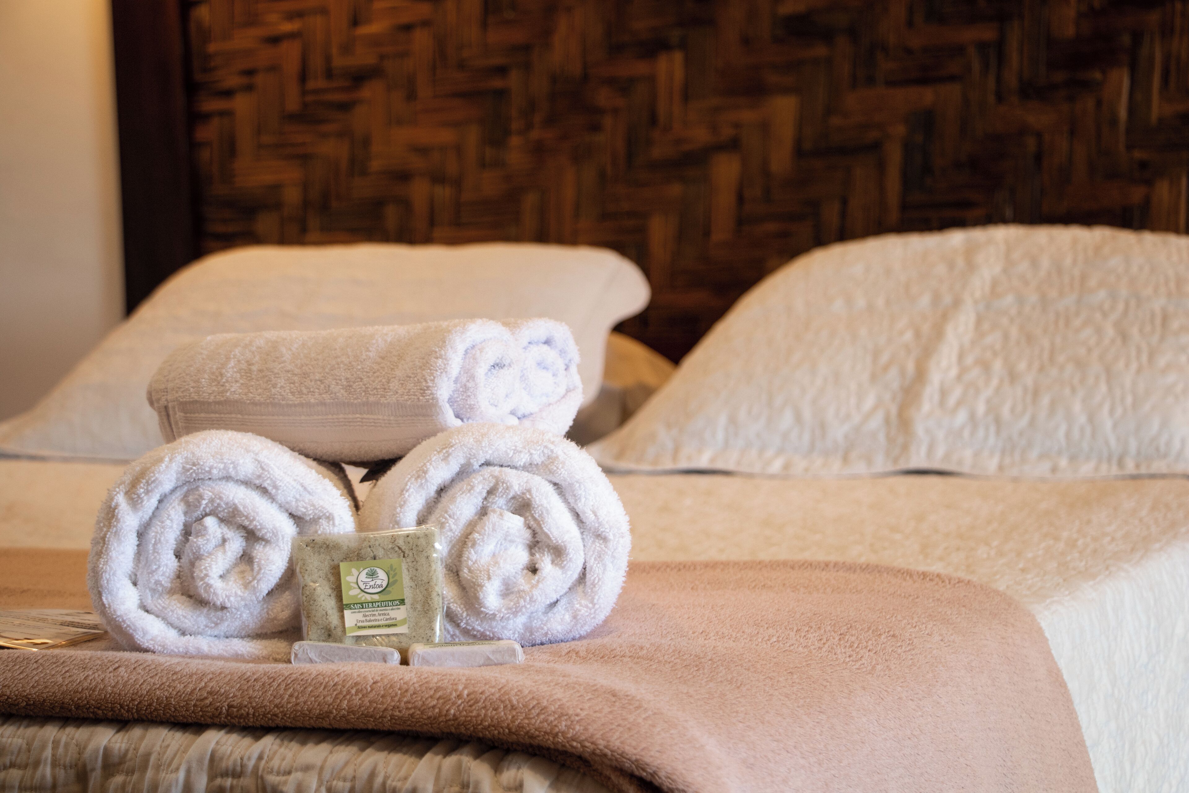 A neatly made bed with rolled white towels and a small bottle of lotion on the bed.