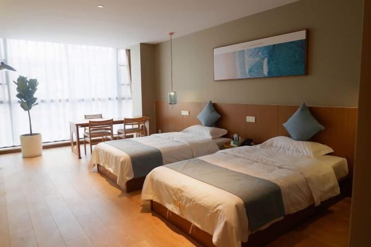 Quarto de hotel com duas camas, uma mesa de jantar, cadeiras, um vaso de planta e um quadro na parede.