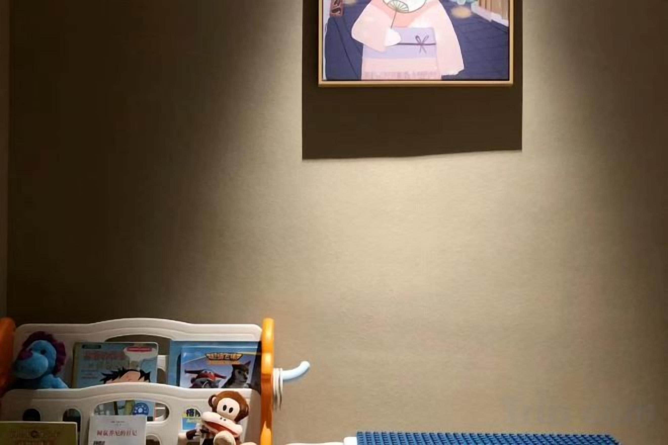 Quarto com televisão na parede, uma mesa pequena com tampo azul e um móvel de armazenamento de brinquedos com personagens de desenho animado.