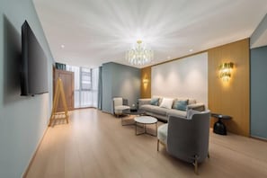 Uma sala de estar moderna com um sofá, poltronas, uma mesa de centro, uma televisão e um candelabro.