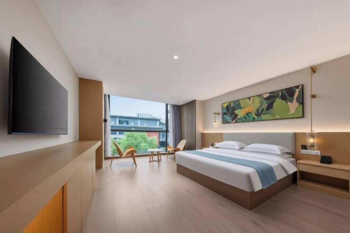 Quarto de hotel moderno com uma cama grande, uma TV de tela plana, um quadro e vista para a cidade.