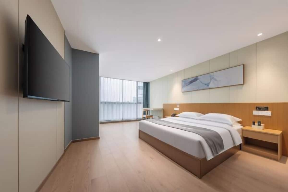 Quarto de hotel moderno com cama grande, mesas de cabeceira, televisão de tela plana e uma janela ampla.