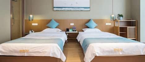 Habitación de hotel con dos camas, cabecero de madera, mesita de noche con lámpara, un cuadro enmarcado con vista al océano y una pequeña planta en la mesita.