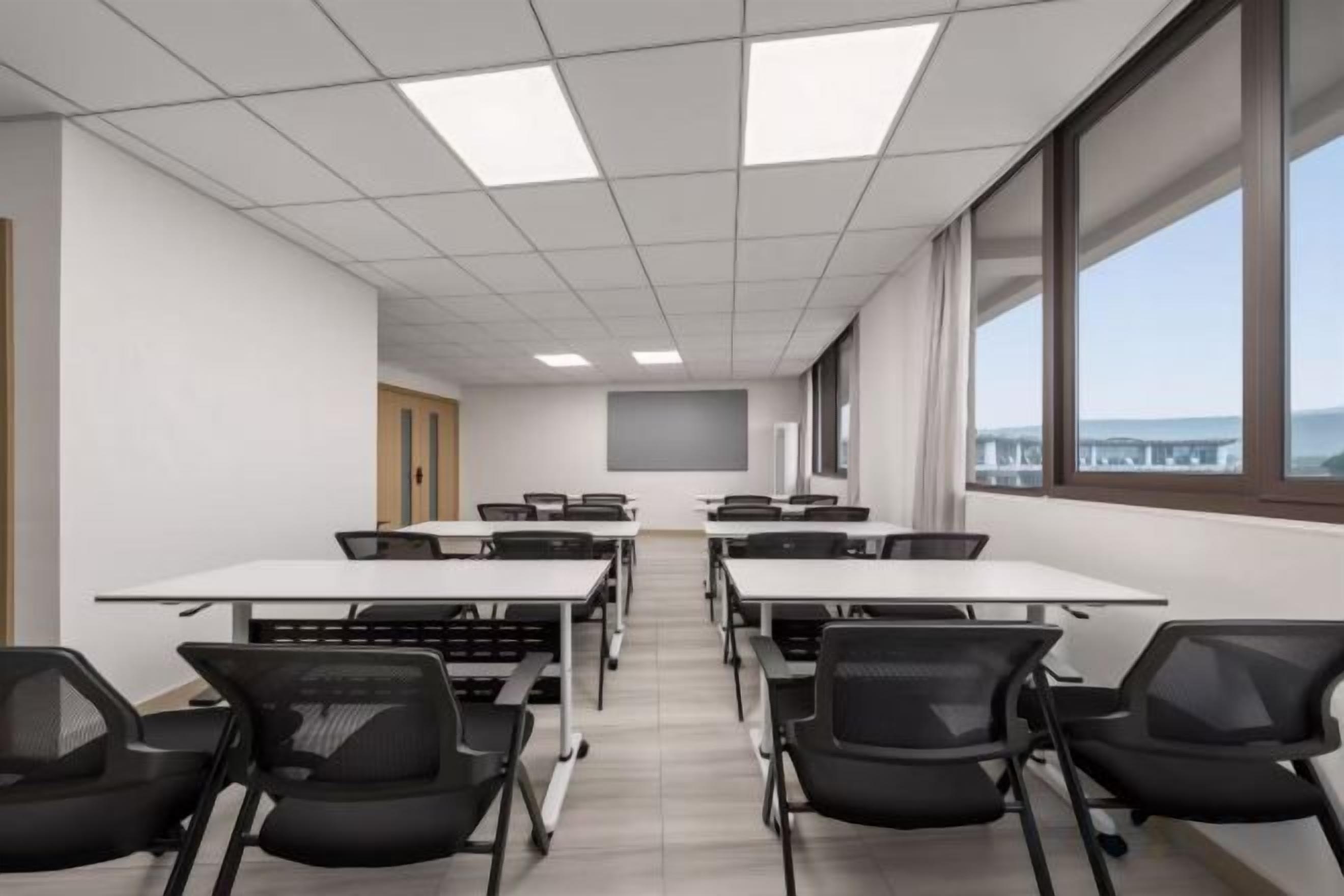 A conference room with tables and chairs, large windows, and a view of the outside.