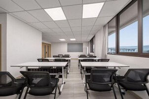 Un salón de conferencias con mesas y sillas, ventanas amplias y vistas al exterior.