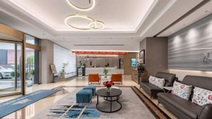 Un hall d’hôtel moderne avec un comptoir d’accueil, un espace salon et une grande fenêtre.