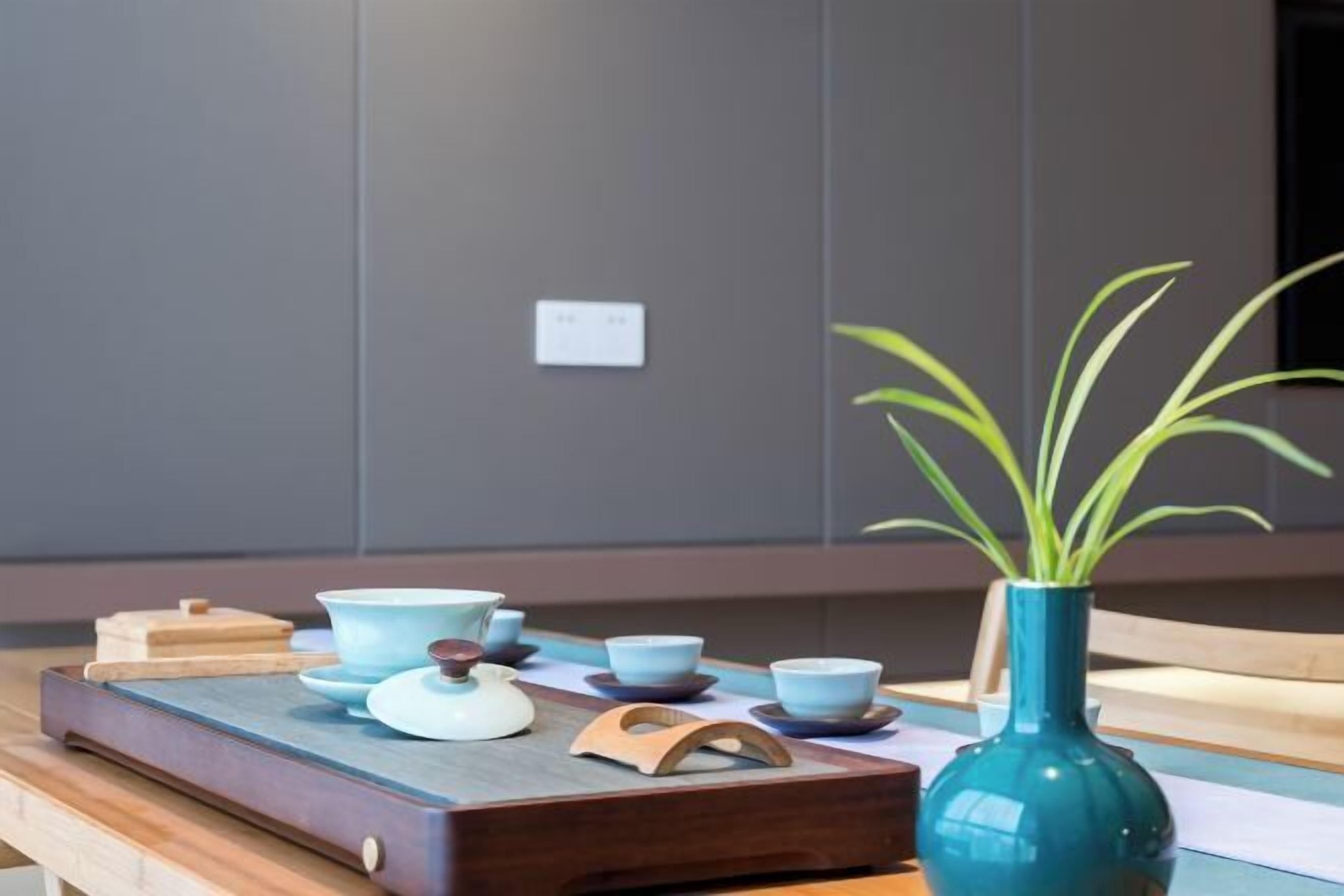 A wooden tray with tea set and a vase with green leaves.