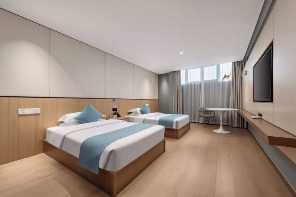 Quarto de hotel com duas camas, uma mesinha, uma televisão e uma janela com cortinas.