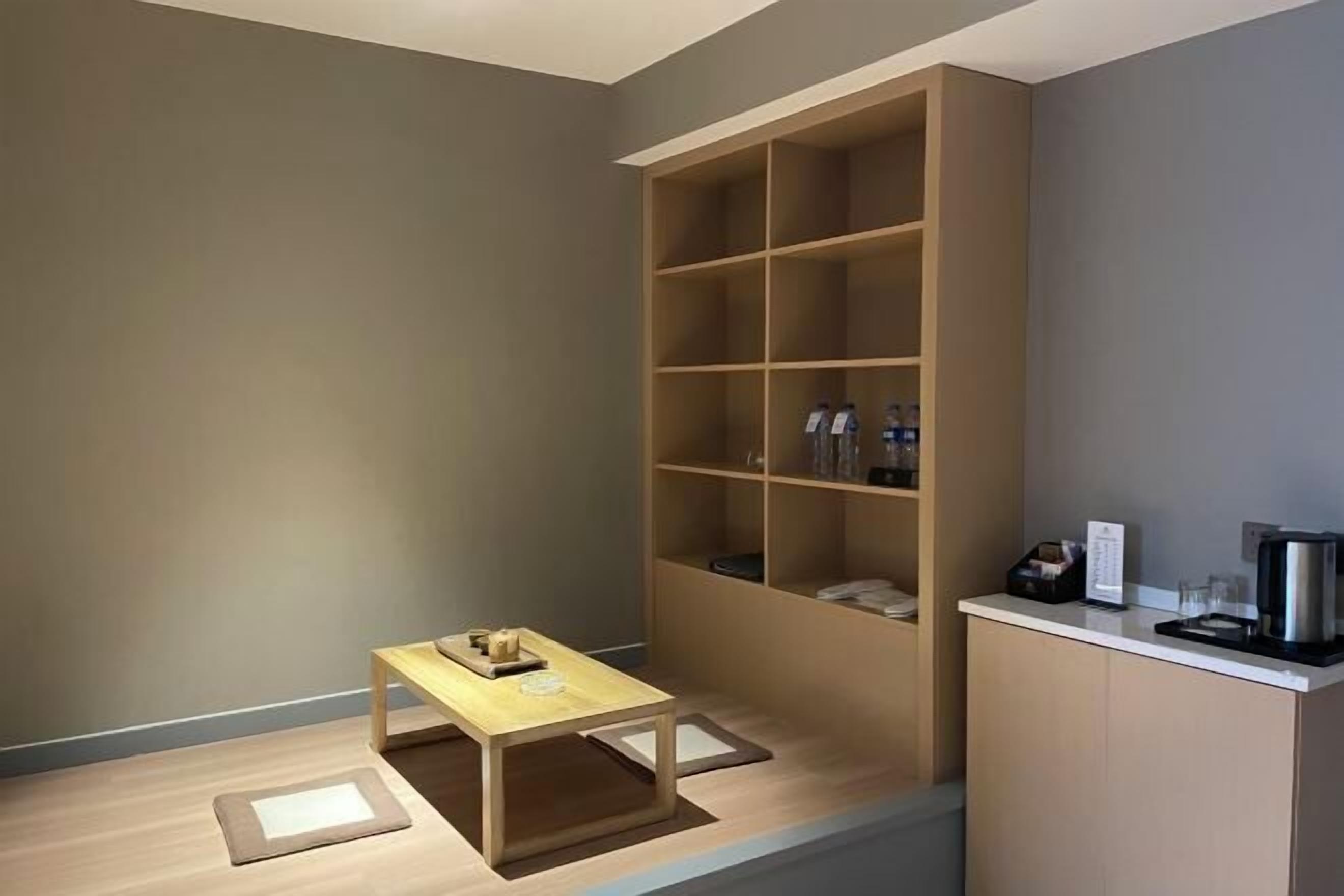 A modern room with a wooden table, a built-in bookshelf, and a kitchenette area.