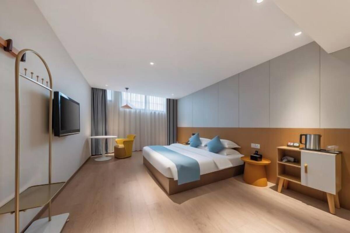 Quarto de hotel moderno com cama, mesa de cabeceira, televisão e um pequeno espaço de estar.
