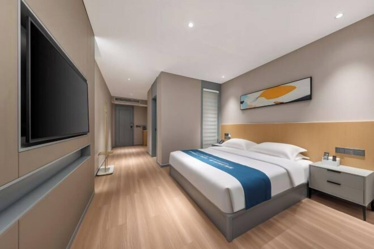 Quarto de hotel moderno com uma cama grande, mesas de cabeceira, uma TV e um quadro na parede.