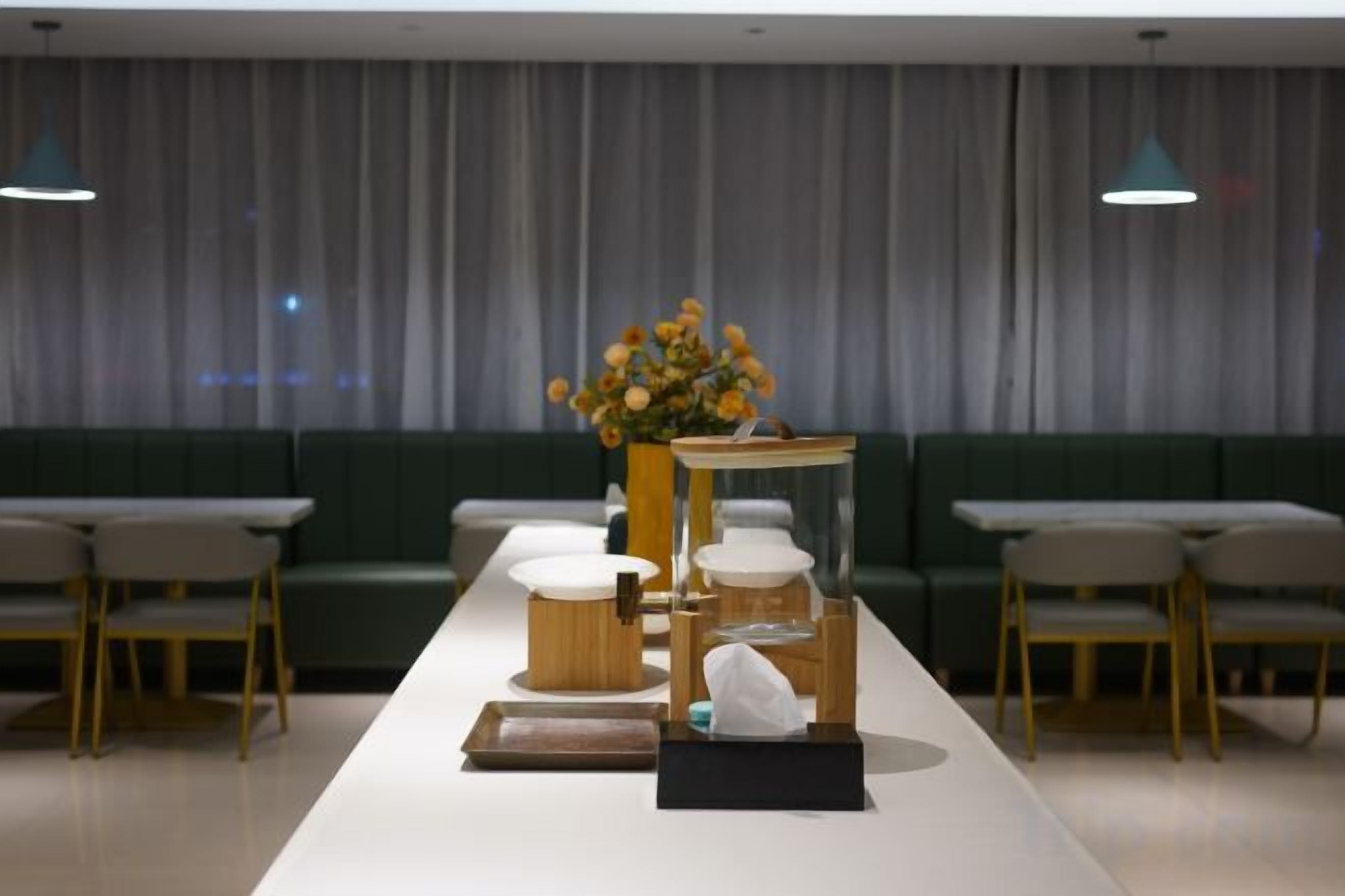 Ett modernt matområde med ett långt bord, stolar, en vas med blommor och en soffa i bakgrunden.