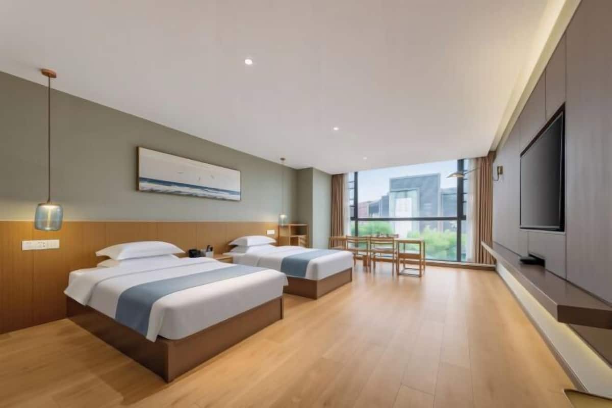 Quarto de hotel com duas camas, uma escrivaninha, uma cadeira, uma televisão e uma janela grande.