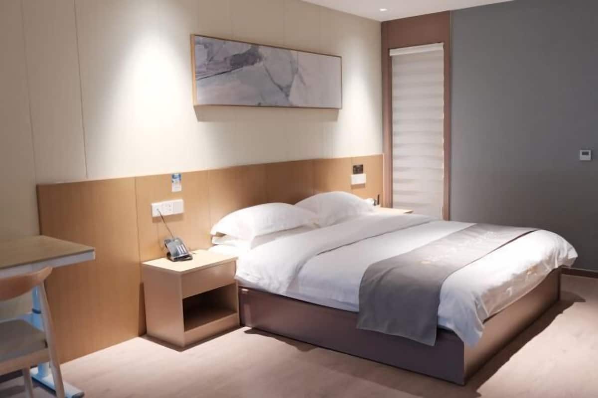 Quarto de hotel moderno com cama, mesa de cabeceira, abajur e um quadro na parede.