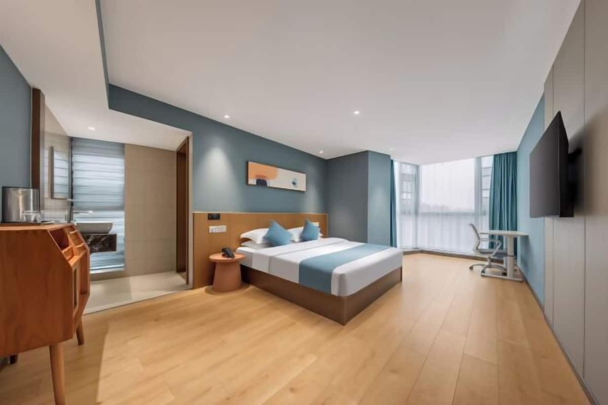 Quarto de hotel moderno com uma cama grande, uma escrivaninha, uma cadeira e uma televisão.