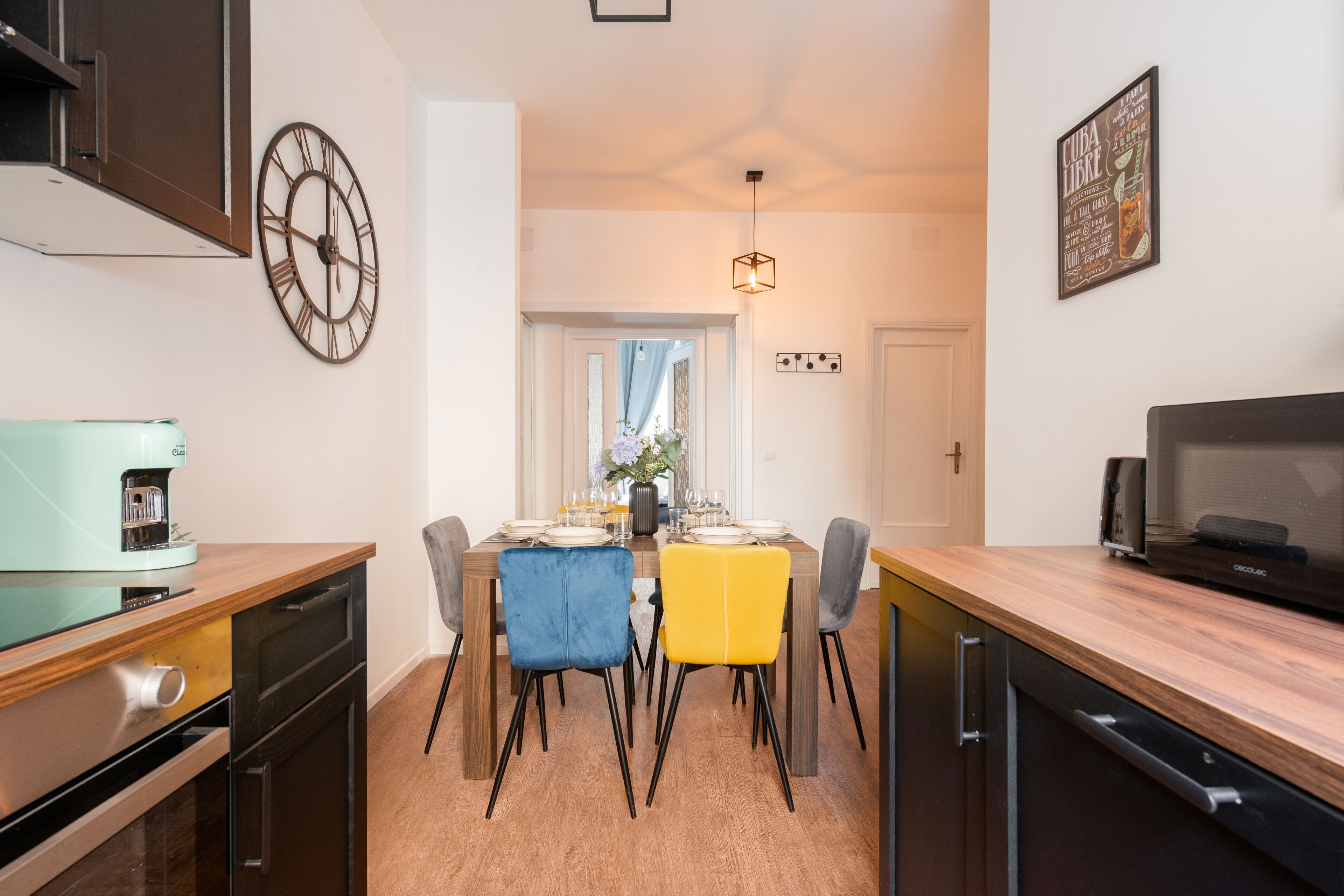 A modern kitchen with a dining area, featuring a coffee machine, a clock, and a microwave.