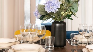 Et spisebord dækket med tallerkener, glas og bestik, samt en vase med blomster og en blå stol.