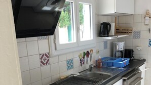 A modern kitchen with white cabinets, a black countertop, a stainless steel dishwasher, and a window with a view of greenery outside. - Maison Fond de Jardin Située à 100 m de la Plage. 2 Chambres Pour 7 Personnes (Mimizan)