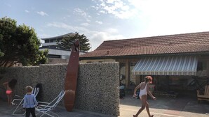 A courtyard with a stone wall, a metal chair, and a tiled-roof building. - Maison Fond de Jardin Située à 100 m de la Plage. 2 Chambres Pour 7 Personnes (Mimizan)