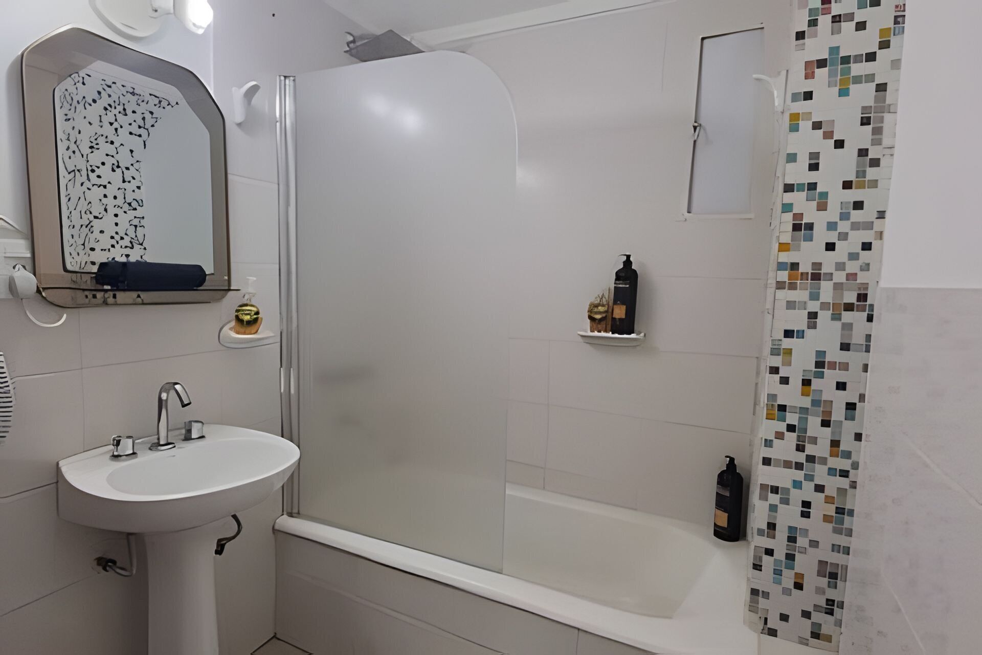 A bathroom with a white sink, a shower with a glass door, and a tiled shower curtain.