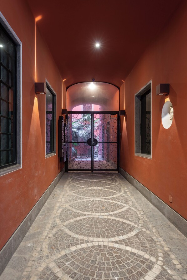 A corridor with a patterned floor, a glass door with a geometric design, and wall-mounted light fixtures.