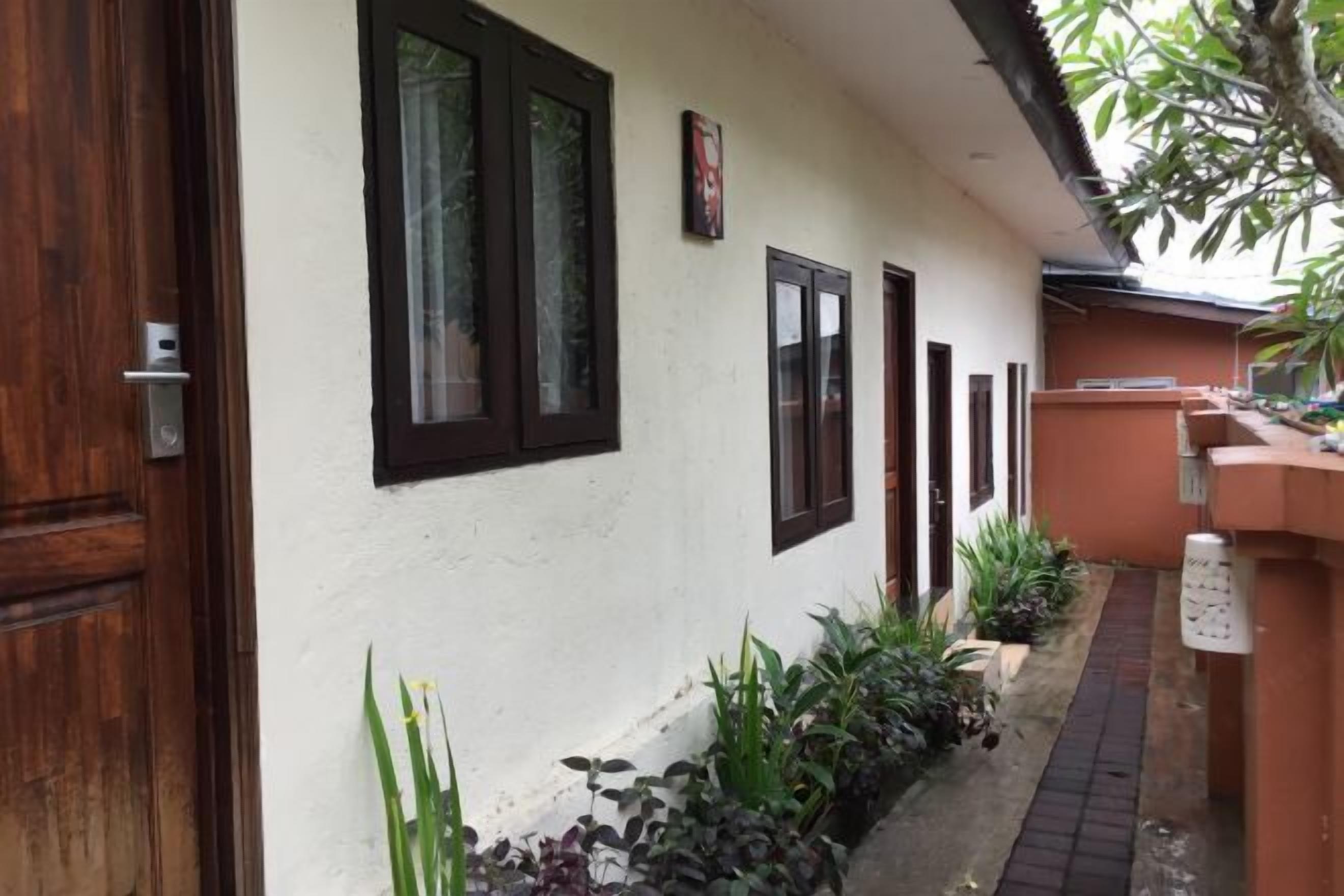 Un sendero estrecho bordeado por un edificio blanco con ventanas de marco oscuro y una puerta de madera.