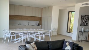 Una sala moderna con un sofá de cuero negro, un comedor con sillas blancas y una cocina con armarios de madera.