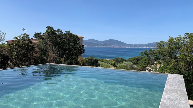 Una piscina infinita transparente con vistas al mar y a las montañas.