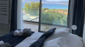 Habitación de hotel con una cama grande, vistas al mar y a las montañas, y un balcón con barandilla de vidrio.