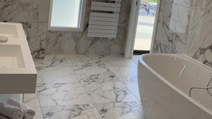 Un baño moderno con suelo de mármol, una bañera independiente y un ventanal con vistas al exterior.