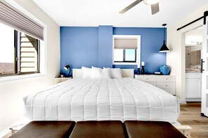 Relax in this serene bedroom with a large bed, window, and door, featuring a bedside table and lamp.