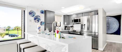 A modern kitchen with a marble island, stainless steel appliances, and a large window with a view of the outdoors.