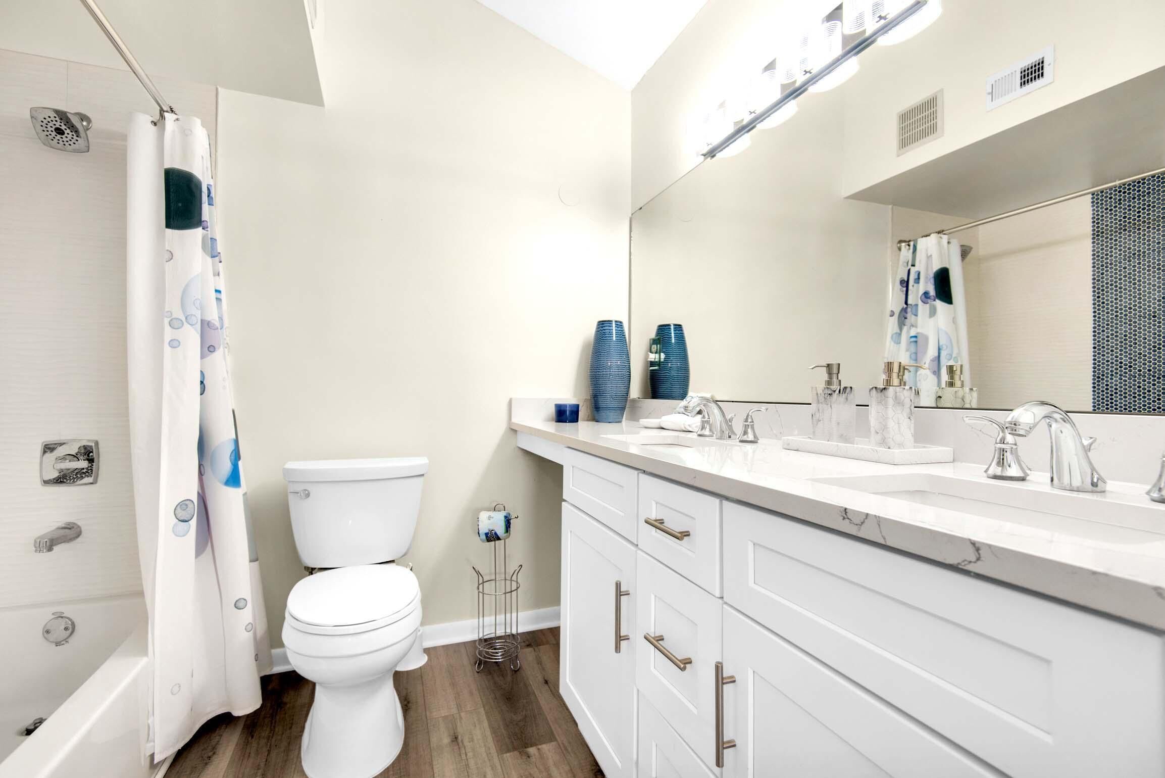 A modern bathroom with a white toilet, a shower with a curtain, a sink with a mirror, and a towel rack.