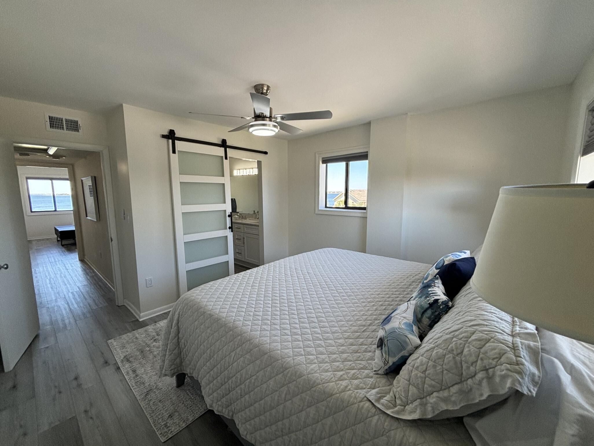 Quarto com cama, ventilador de teto, janela e porta para um banheiro.