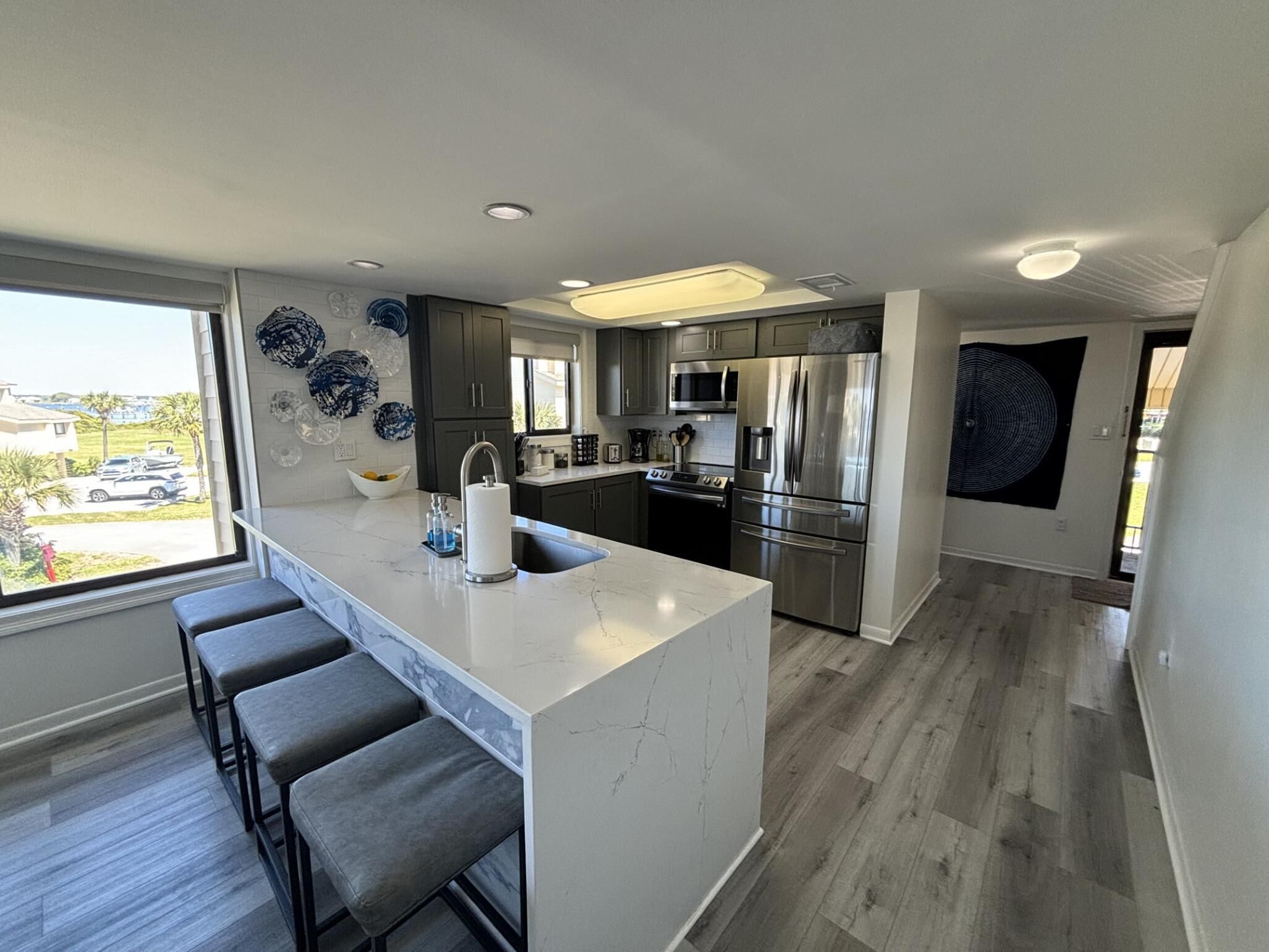 A modern kitchen with a central island, dark cabinets, stainless steel appliances, and a view of the outdoors.