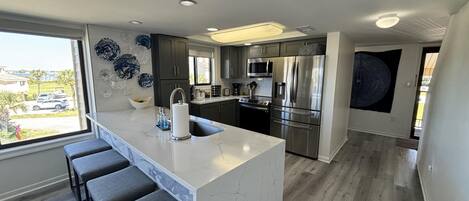 A modern kitchen with a central island, dark cabinets, stainless steel appliances, and a view of the outdoors.