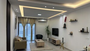 Uma sala de estar moderna com sofá, mesa de centro, televisão e prateleiras decorativas.