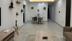 Uma sala de estar moderna com área de jantar, apresentando uma TV de tela plana, uma mesa de centro e um sofá.