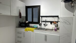 Uma cozinha com armários brancos, micro-ondas preto, pia com torneira e janela com moldura preta.