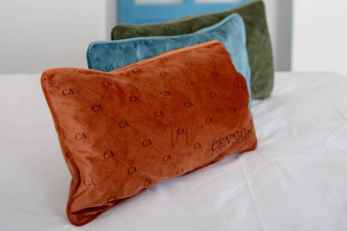 Un lit avec trois oreillers aux couleurs orange, bleu et vert, et une porte bleue en arrière-plan.