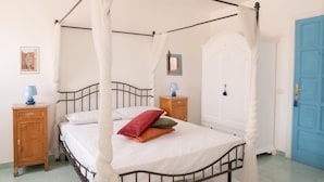 A four-poster bed with a white canopy, a wooden nightstand with a lamp, a blue door, and a floral-patterned rug. - Ischia Mare (Forio)