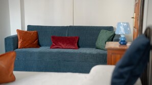 A living room with a blue sofa, three pillows, a small table with a lamp, and a white chair. - Ischia Mare (Forio)