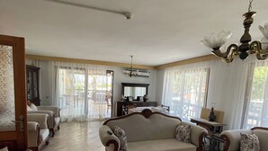 A spacious living room with a large sofa, a dining table, and a chandelier. - Bedesten Pansiyon (Cesme)