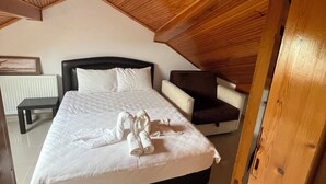 A bedroom with a sloped ceiling, a bed with white linens, a bedside table, and a chair. - Bedesten Pansiyon (Cesme)