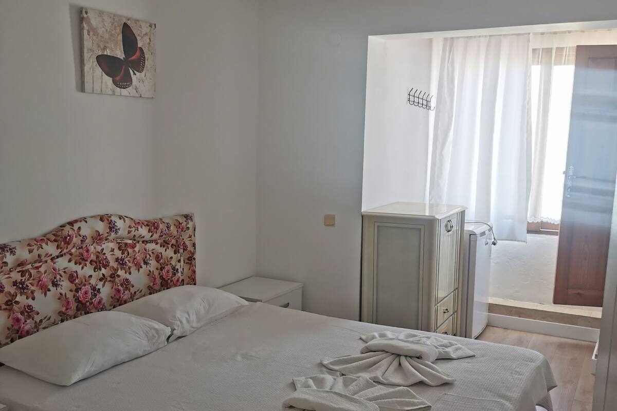 A bedroom with a bed, a nightstand, a dresser, a ceiling fan, a butterfly painting, and a view through a door.